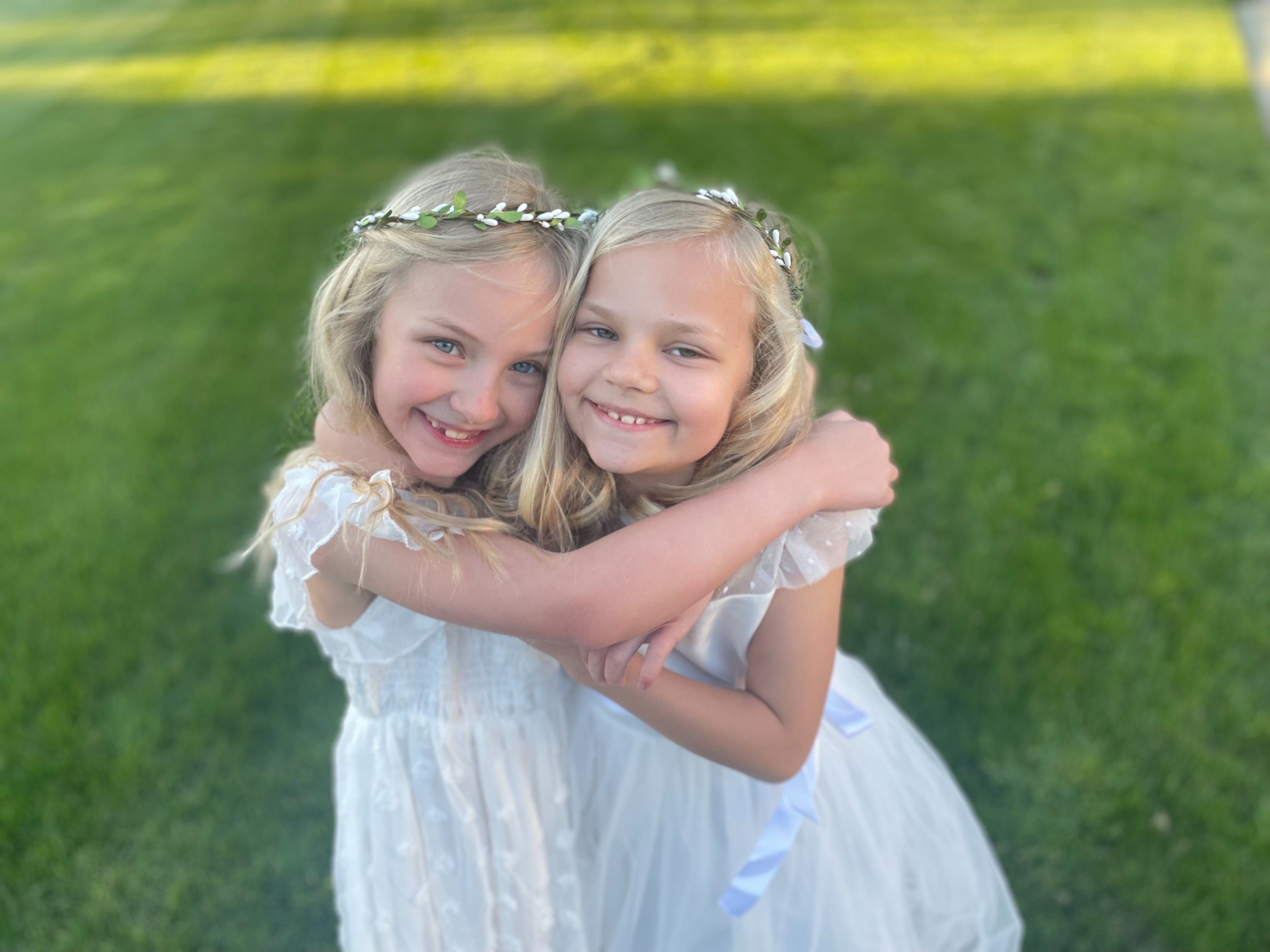 Hazel and her twin sister Ivy hugging in white dresses and flower crowns