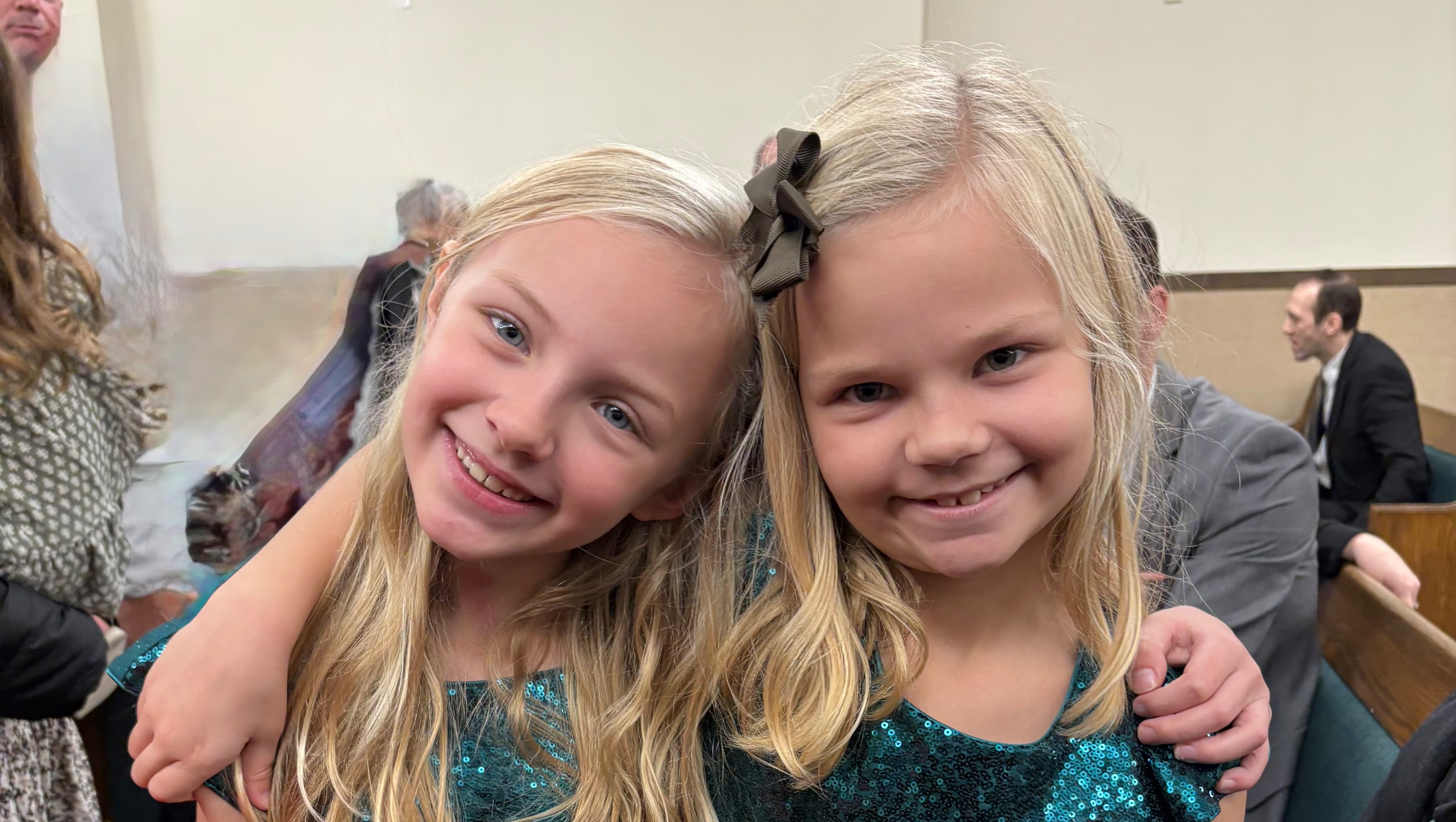 Hazel and her twin sister Ivy, cheek to cheek in sparkly teal dresses