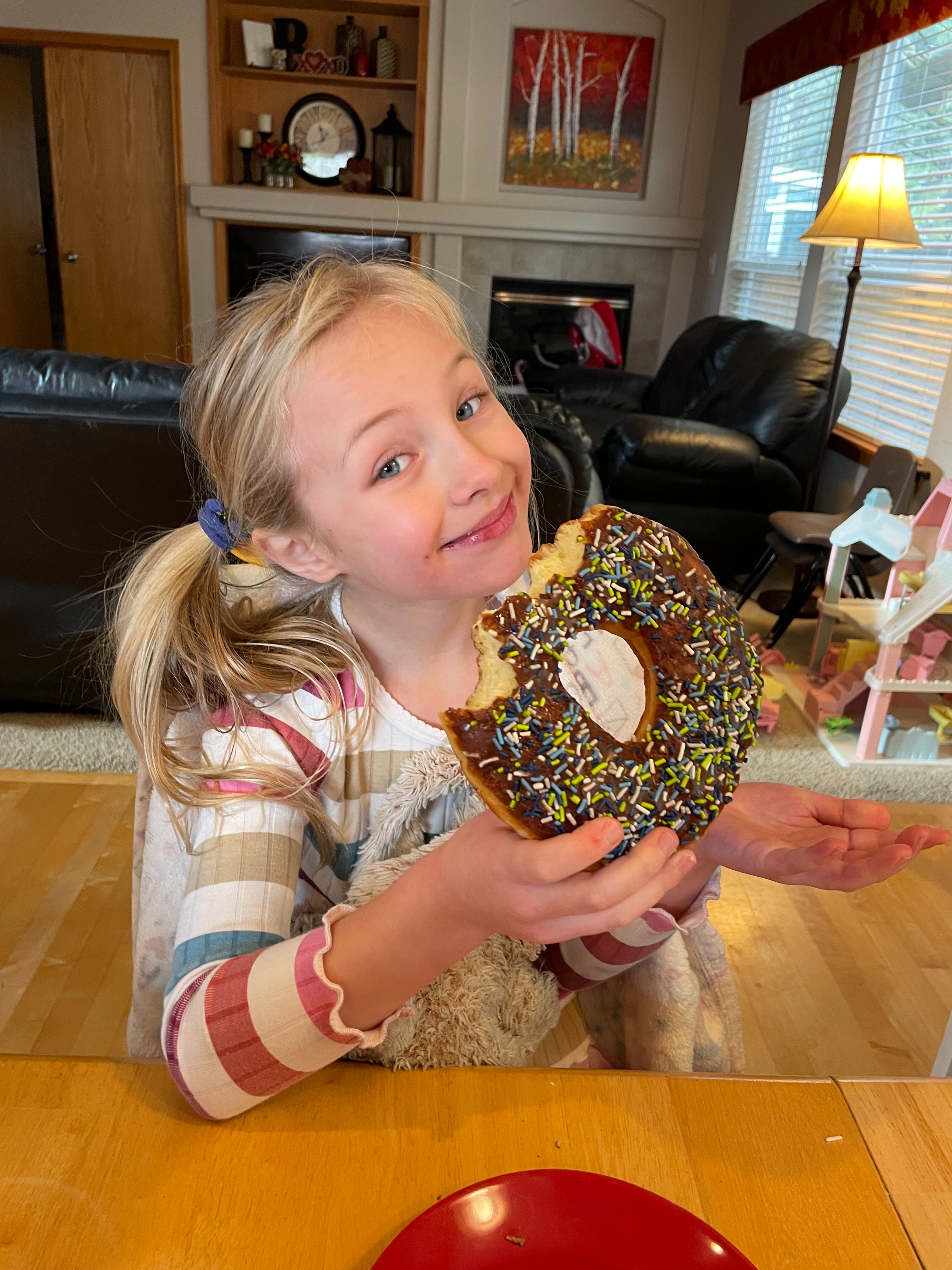 Hazel grinning behind an enormous chocolate-sprinkle doughnut